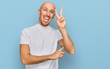 Bald man with beard wearing casual white t shirt smiling with happy face winking at the camera doing victory sign. number two.