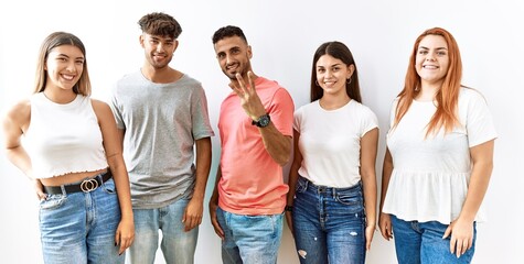 Group of young friends standing together over isolated background showing and pointing up with fingers number three while smiling confident and happy.