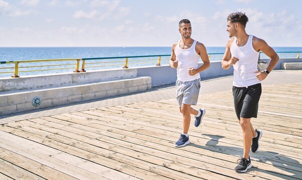 Two hispanic men sporty couple smiling confident running at seaside