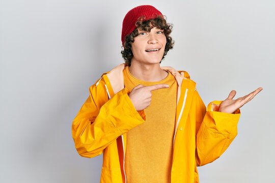 Handsome young man wearing yellow raincoat amazed and smiling to the camera while presenting with hand and pointing with finger.