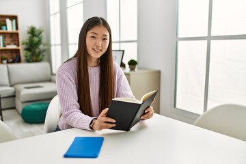 Young chinese girl reading book sitting on the table at home.