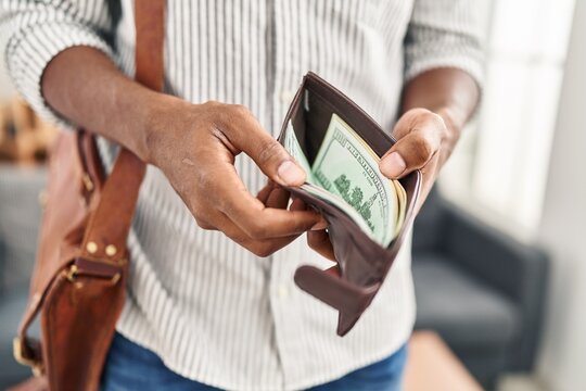 Young african american man psychologist wearing briefcase holding wallet with money at clinic