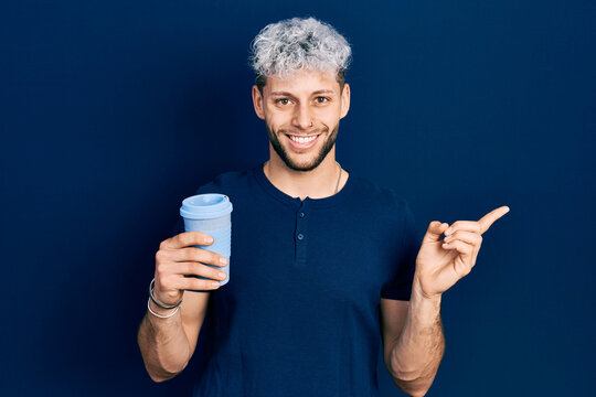 Young hispanic man with modern dyed hair drinking a take away cup of coffee smiling happy pointing with hand and finger to the side