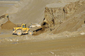 A yellow wheel loader is working in gravel pit