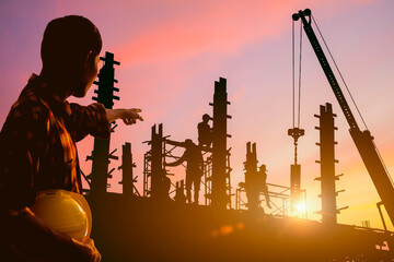 Silhouette of Engineer and worker on building site, construction site with the sunset in the evening as the background.