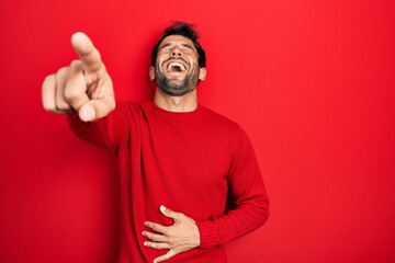 Handsome man with beard wearing casual red sweater laughing at you, pointing finger to the camera...