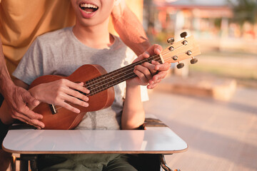Hand of young man with disability holding ukulele and singing, playing with music therapy on the outdoor nature background,Vacation hobby activity with family activity and mental health concept.