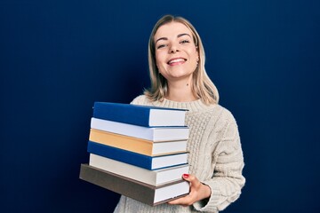 Beautiful caucasian woman holding a pile of books smiling and laughing hard out loud because funny crazy joke.