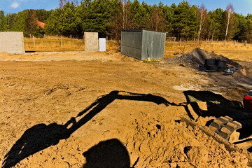 Plac budowy - cień ramienia i łyżki koparki na tle świeżo rozrzuconej ziemi .