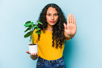 Young hispanic woman holding a plant isolated on blue background standing with outstretched hand...