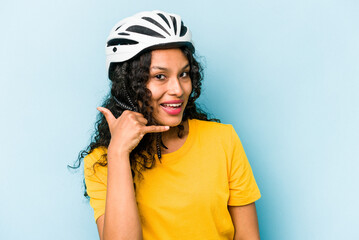 Young hispanic woman wearing a helmet bike isolated on blue background showing a mobile phone call gesture with fingers.