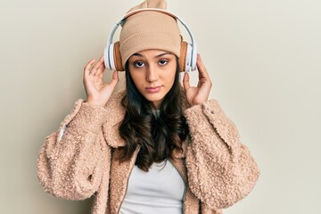 Young hispanic woman listening to music using headphones skeptic and nervous, frowning upset because of problem. negative person.