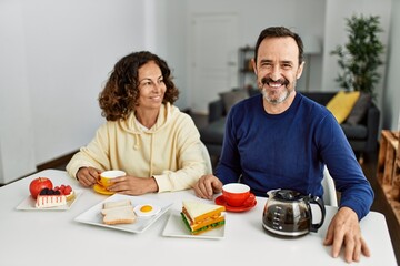 Middle age hispanic couple smiling happy sitting on the table having breakfast at home.