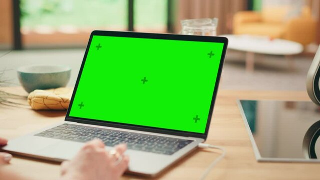 Close Up Green Screen Mock Up on a Laptop Computer. Device is Used on a Kitchen Table in a Modern Home. Person Uses Touch Pad for Scrolling the Web. Sunny Modern Kitchen with Healthy Lifestyle Vibes.