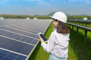 Fototapeta premium Female engineer wearing helmet in Photovoltaic Cell Farm or Solar Panels Field, eco friendly and clean energy.