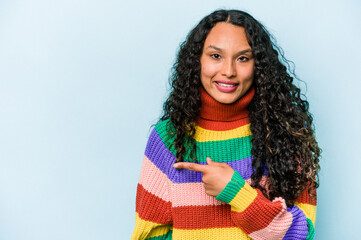 Young hispanic woman isolated on blue background smiling and pointing aside, showing something at blank space.