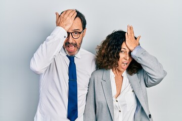 Middle age couple of hispanic woman and man wearing business office uniform surprised with hand on head for mistake, remember error. forgot, bad memory concept.
