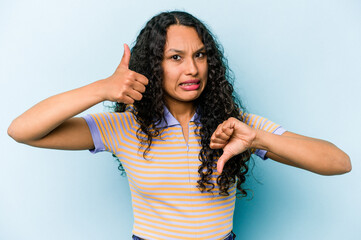 Young hispanic woman isolated on blue background showing thumbs up and thumbs down, difficult...