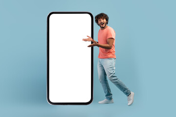 Amazed hindu guy posing by huge smartphone with blank screen