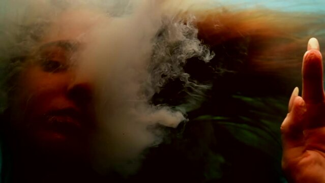 mysterious woman is breathing by white smoke and swimming underwater, closeup of pretty face