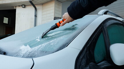 Closeup of femal hand holding plastic brush and scraping ice out off windshield white car. Clearing...