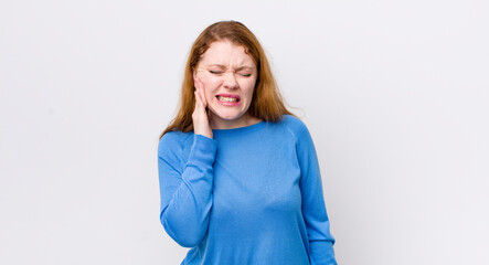 pretty red head woman holding cheek and suffering painful toothache, feeling ill, miserable and...