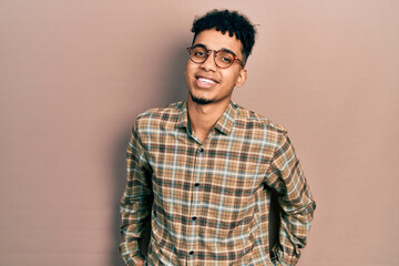 Young african american man wearing casual clothes and glasses looking positive and happy standing and smiling with a confident smile showing teeth