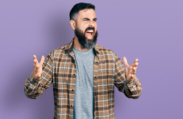 Hispanic man with beard wearing casual shirt crazy and mad shouting and yelling with aggressive...