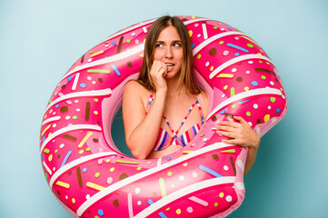 Young caucasian woman holding air mattress isolated on blue background biting fingernails, nervous and very anxious.