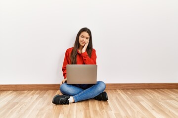 Young brunette woman sitting on the floor at empty room with laptop thinking looking tired and bored with depression problems with crossed arms.