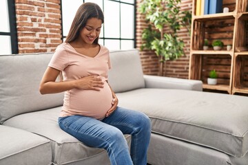 Young latin woman pregnant smiling confident sitting on sofa at home