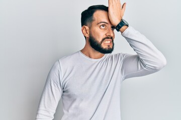 Young man with beard wearing casual white shirt surprised with hand on head for mistake, remember error. forgot, bad memory concept.