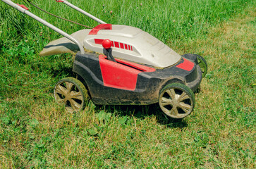 Fototapeta na wymiar Electric hand lawn mower mows the grass. Close-up. Side view.