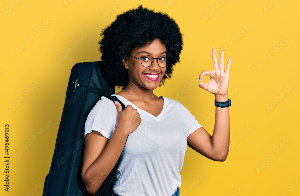 Sticker Young african american woman wearing guitar case doing ok sign with fingers, smiling friendly gesturing excellent symbol