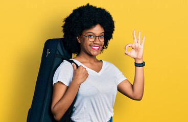Young african american woman wearing guitar case doing ok sign with fingers, smiling friendly gesturing excellent symbol