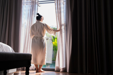 Obraz na płótnie Canvas Young asian female woman stand open white curtains sheer at the window, the morning after waking up in the bedroom hotel. Woman wake up with a fresh and open the curtains on the windows.