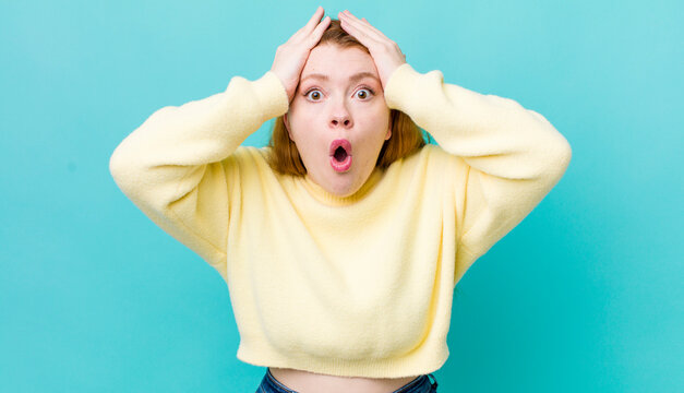 pretty red head woman looking unpleasantly shocked, scared or worried, mouth wide open and covering both ears with hands
