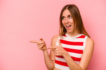 Young caucasian woman isolated on pink background points with thumb finger away, laughing and carefree.