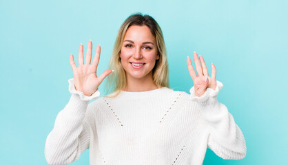pretty blonde woman smiling and looking friendly, showing number nine or ninth with hand forward,...
