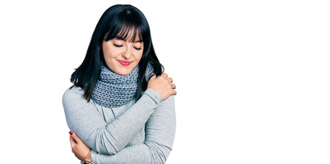 Young hispanic plus size woman wearing winter scarf hugging oneself happy and positive, smiling...