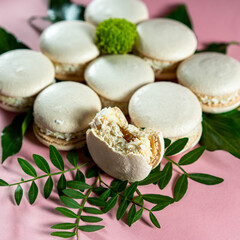 Fresh white macaroons with caramel and coconut on a pink background. Decorate with green leaves and flowers 