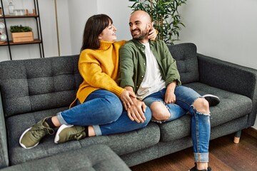 Fototapeta premium Young hispanic couple smiling happy and hugging sitting on the sofa at home.