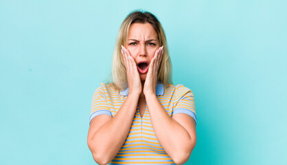 pretty blonde woman feeling shocked and scared, looking terrified with open mouth and hands on...