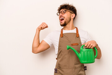 Young gardener hispanic man holding a watering can isolated on white background raising fist after a victory, winner concept. © Asier