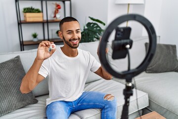 African american man recording vlog tutorial about bitcoin with smartphone at home surprised with...