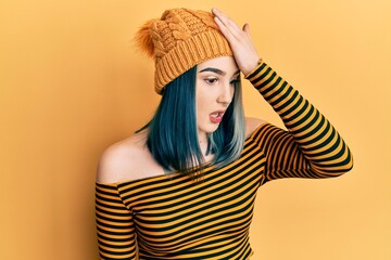 Young modern girl wearing wool hat surprised with hand on head for mistake, remember error. forgot,...
