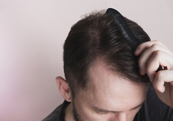 Man сombing hair on pastel beige background. Healthy hair, care concept. Closeup, top view, copy...