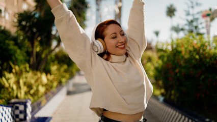 Young redhead woman listening to music and dancing at park