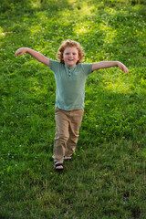 full length view of happy boy with outstretched hands walking on green lawn.