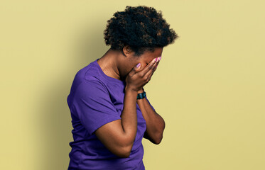 African american woman with afro hair wearing casual purple t shirt with sad expression covering face with hands while crying. depression concept.